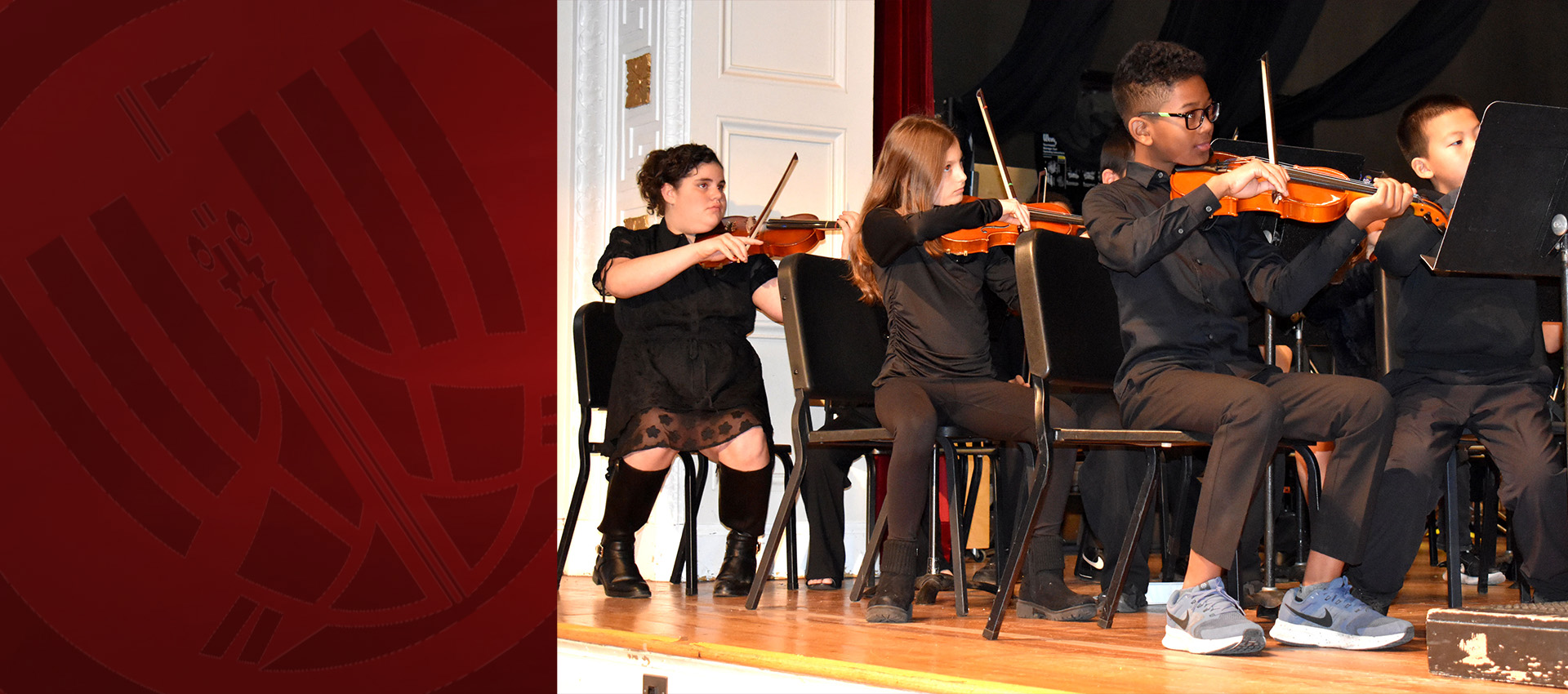 Students dressed in black perform on stage while playing violins in a school orchestra concert.