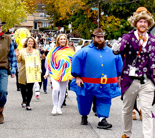 People in colorful Halloween costumes walking in a festive parade.