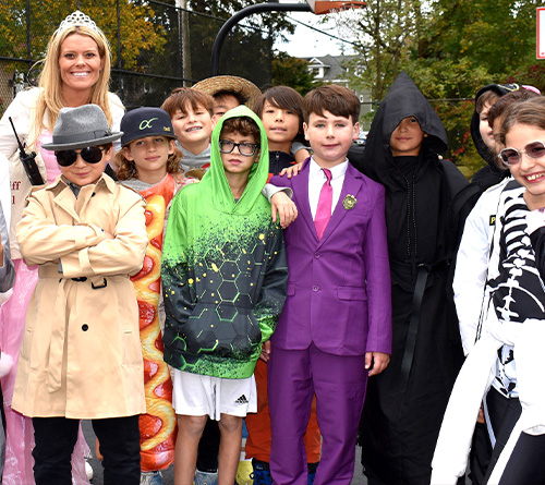A group of children and an adult dressed in various Halloween costumes posing and smiling outdoors.
