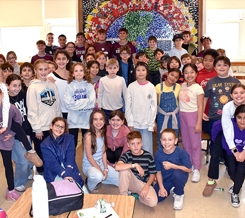 Group of smiling students posing together in front of a colorful mural.