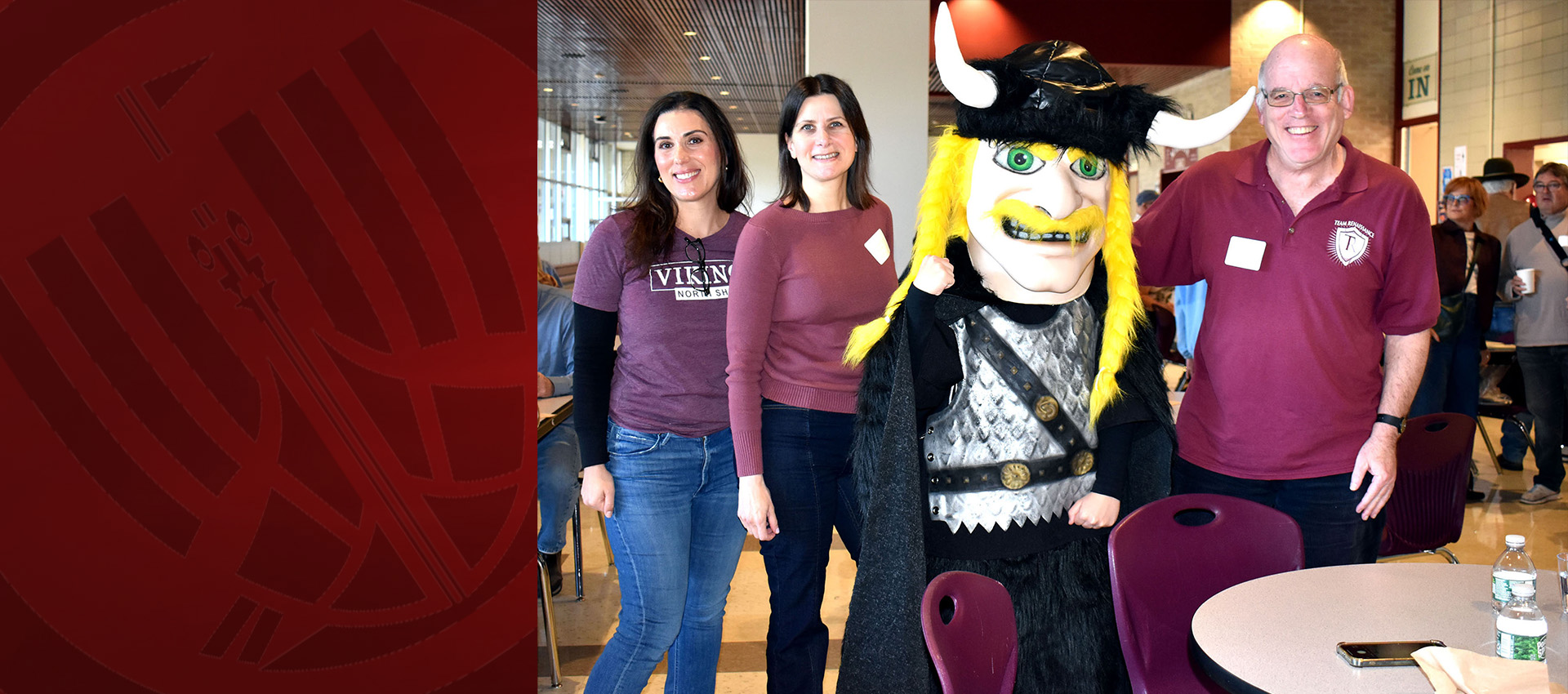 Three adults pose with a Viking mascot during an alumni event.