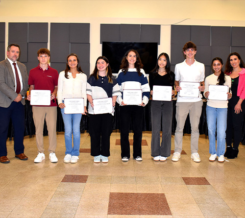 Group of students and staff posing with certificates during an award recognition event.