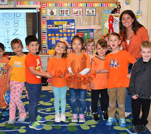 Students and their teacher wear orange for Unity Day, smiling and holding a paper chain in their classroom.
