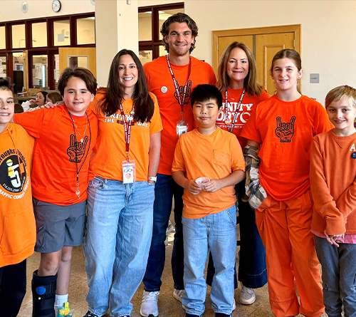Students and teachers wear orange for Unity Day, standing together and smiling in a school cafeteria.