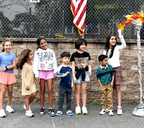 Children lined up outdoors as one student lights a symbolic torch.