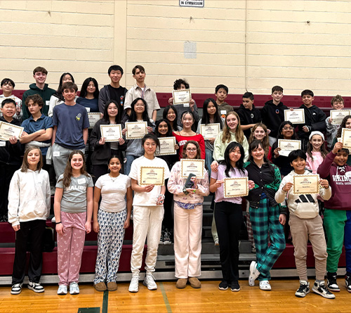 Group of students in a school gym holding certificates and posing together for an awards photo.