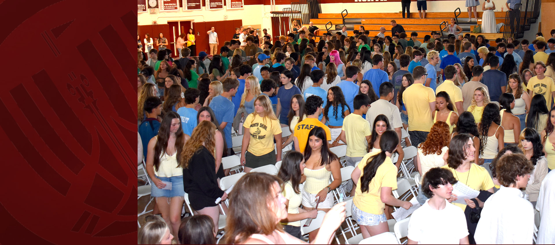 A large group of high school students gathered in a gymnasium, standing between rows of white chairs during a school event.
