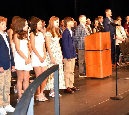 Students and school staff stand on stage during a middle school moving-up ceremony
