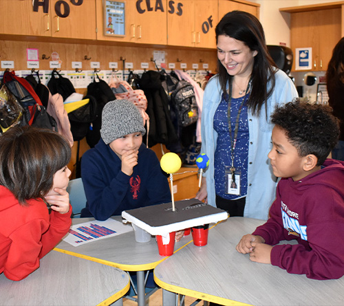 Teacher and students observing a small solar system model during a classroom science activity.