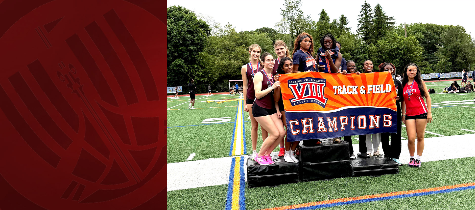 Girls track and field team posing with a championship banner and medals on a sports field.