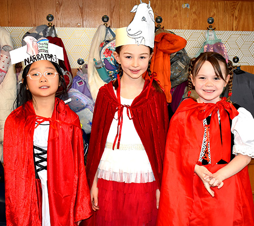 Group of smiling children and a teacher wearing orange clothes posing together in a school cafeteria.